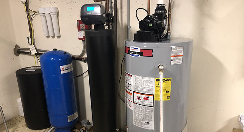 A water heater and tank in the corner of a room.